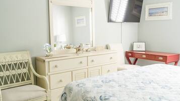 Une chambre à coucher comprenant un lit, une commode, une coiffeuse, un miroir, un téléviseur et un tableau encadré accroché au mur.