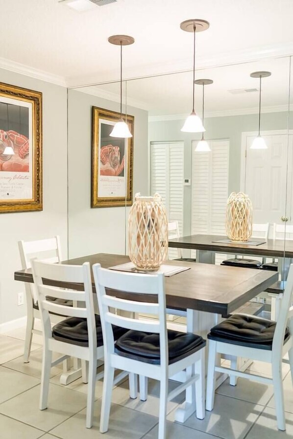 A dining area with a rectangular table, white chairs with black cushions, pendant lights, and framed artwork on the walls.