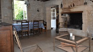 Una habitación rústica con chimenea de piedra, mobiliario de madera y un comedor con mesa y sillas.