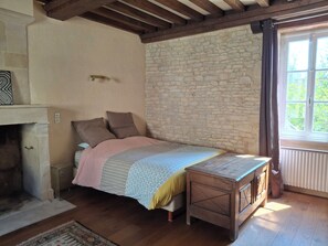 Une chambre avec un mur en pierre, un lit avec une literie à motifs, une table de chevet en bois, une cheminée et une fenêtre avec des rideaux.