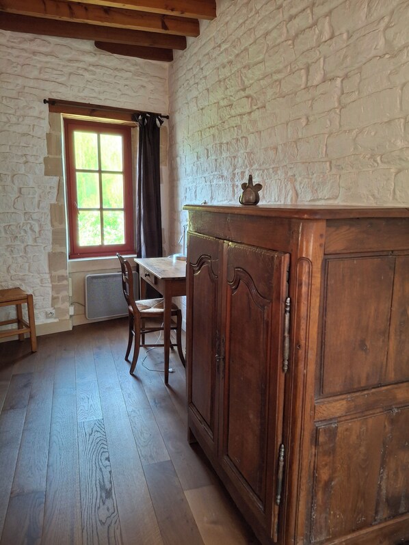 A room with a wooden table, chairs, a cabinet, a window with curtains, and a stone wall.