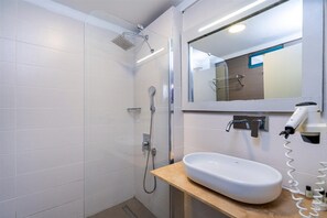 A modern bathroom with white tiles, a built-in sink, a shower, and a mirror with a light above it. - CLUB BELLAMARE  BEACH (Marmaris)