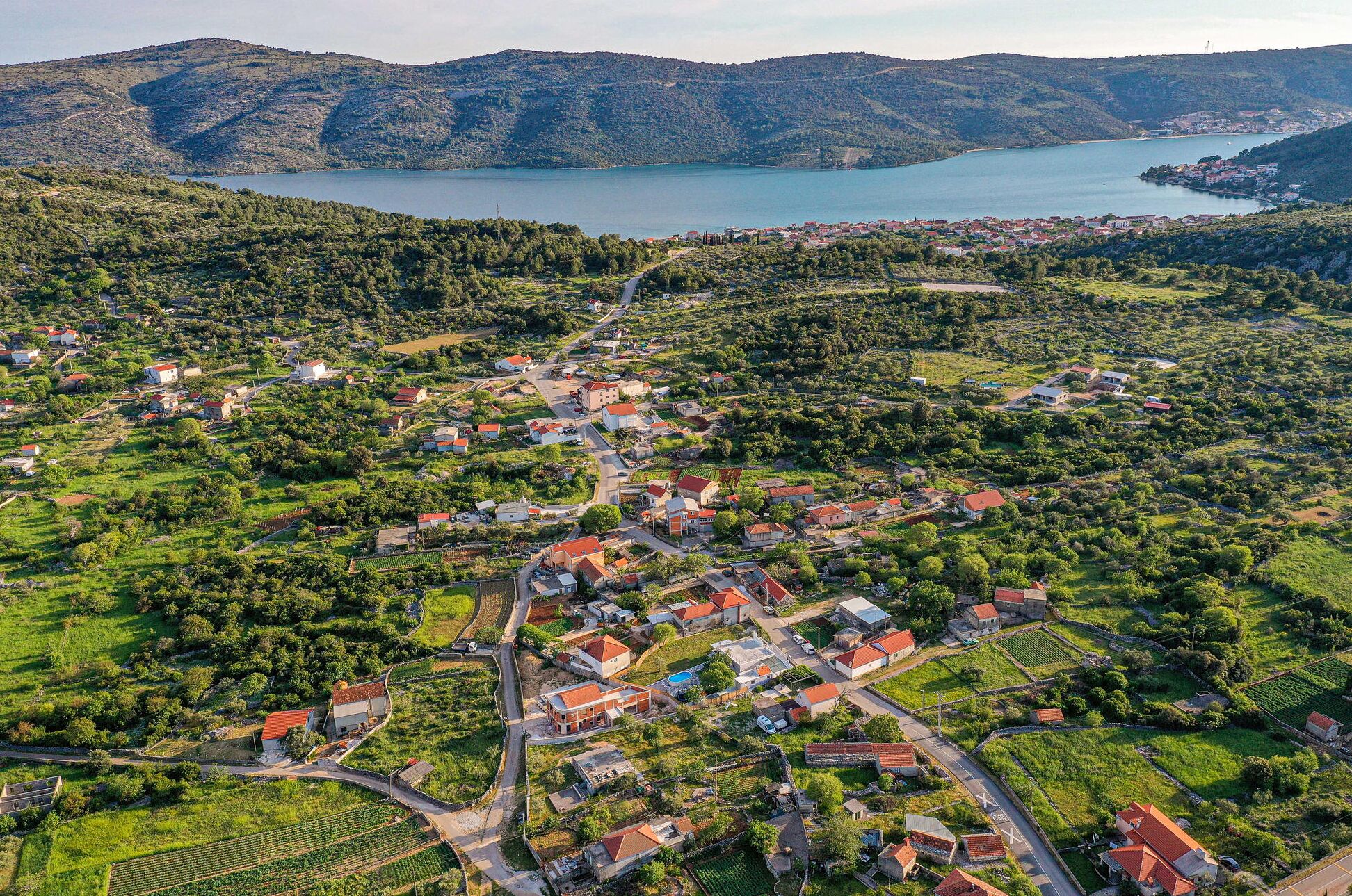 An aerial view of a coastal village with houses, roads, and a lake.