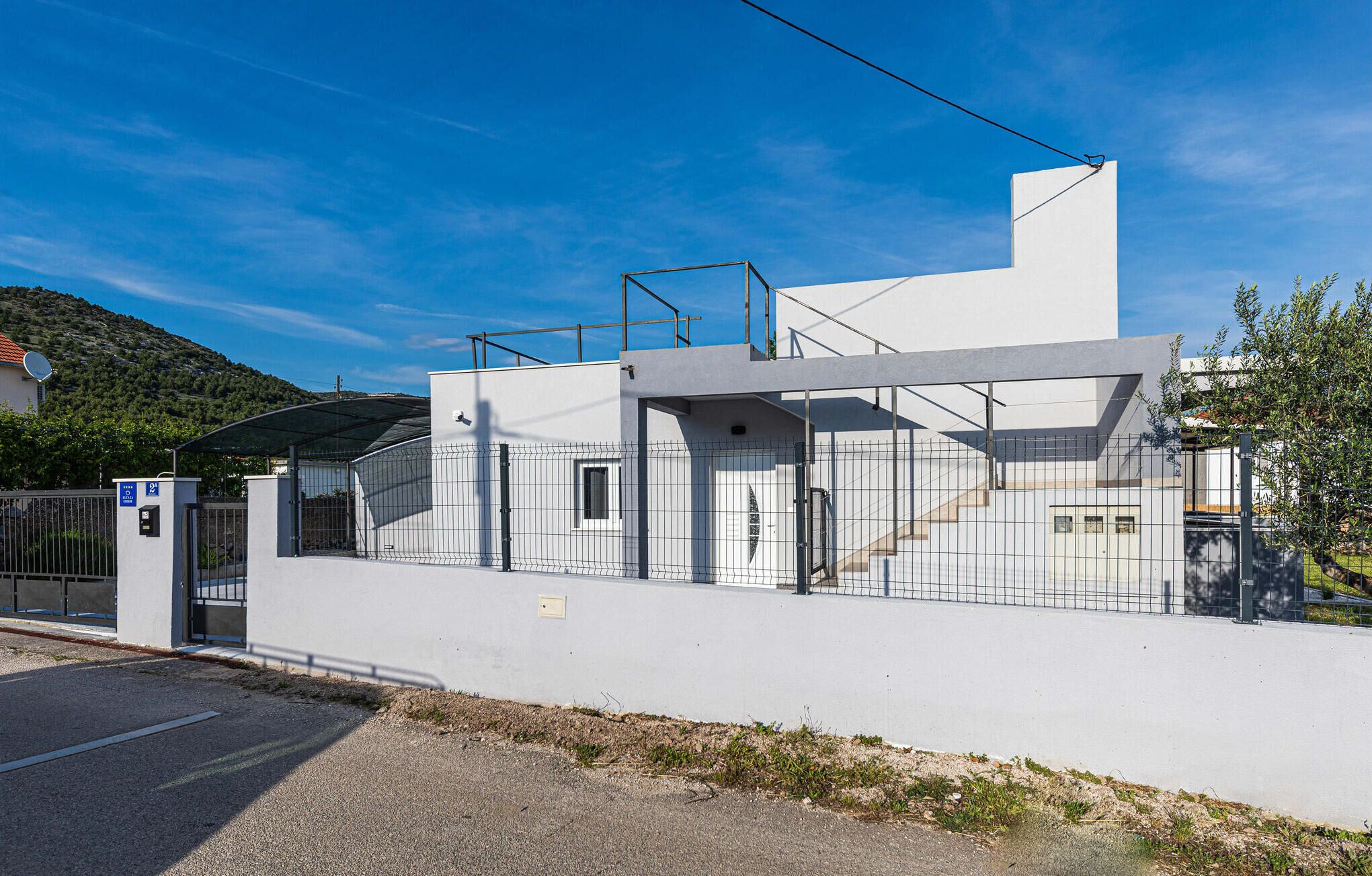 Un edificio moderno con techo plano, entrada protegida por un portón y una antena parabólica a la izquierda.