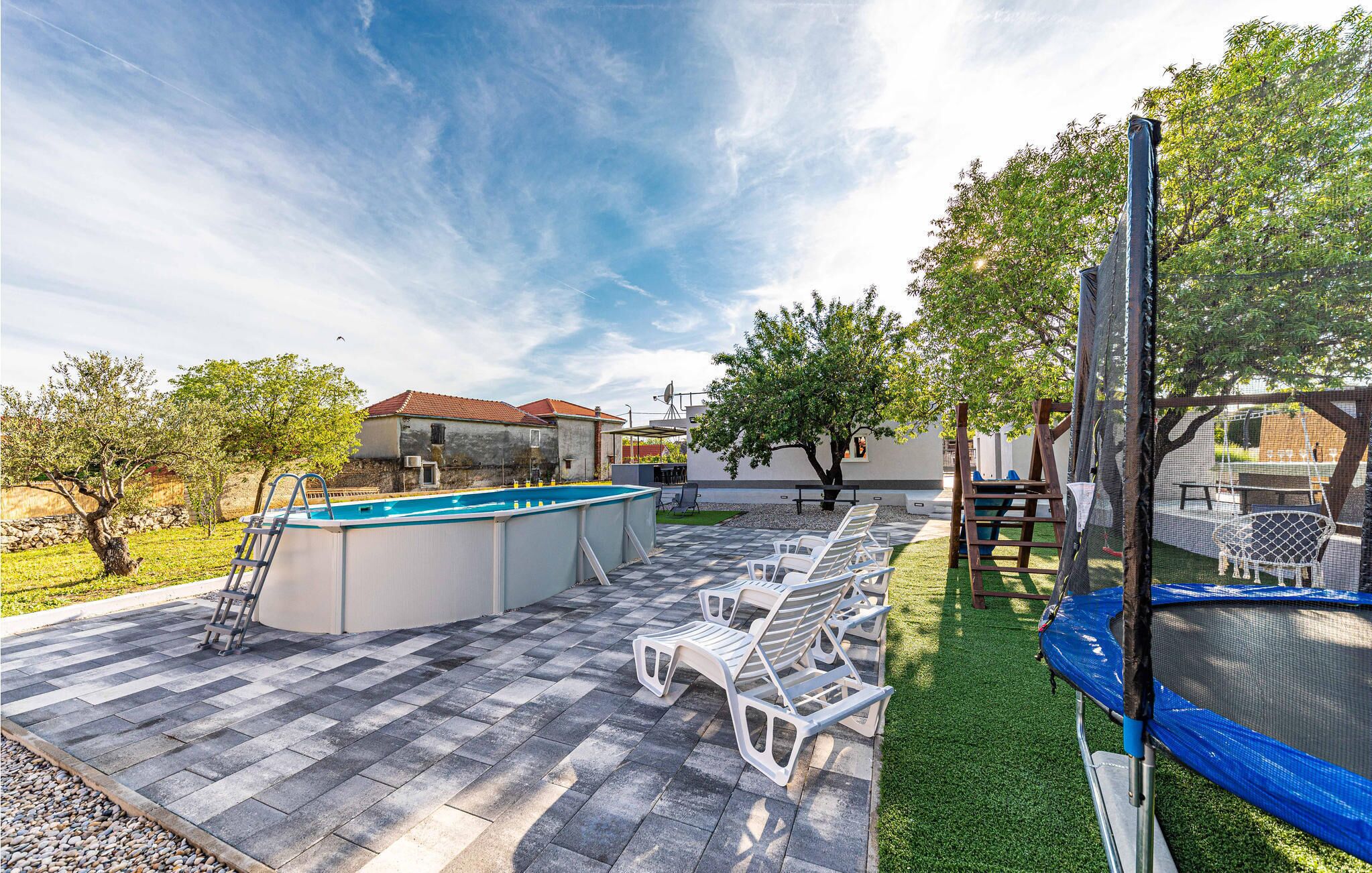 Un espace piscine comprenant des chaises longues, une petite piscine et un trampoline.