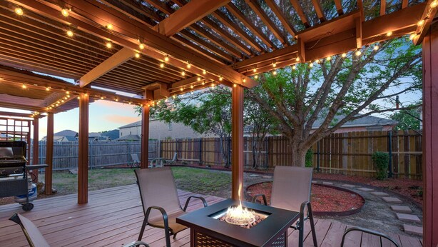 A covered patio with a fire pit, wooden deck, and string lights. - Epic Fun Luxury 4 BR in DFW w/ Casino & Lounge! (Grand Prairie)