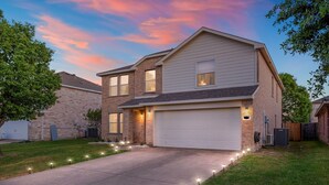 A two-story house with a garage, a well-maintained lawn, and a driveway with outdoor lighting. - Epic Fun Luxury 4 BR in DFW w/ Casino & Lounge! (Grand Prairie)