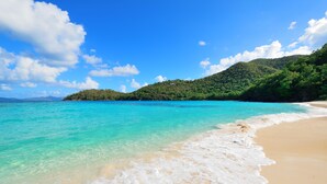 Una spiaggia con acque turchesi trasparenti, una riva sabbiosa e una collina verdeggiante sullo sfondo.
