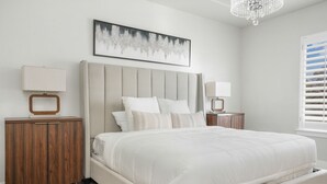 A bedroom with a bed, bedside tables, a cabinet, a chandelier, and a window with blinds. - Family Oasis Getaway (Lehi)