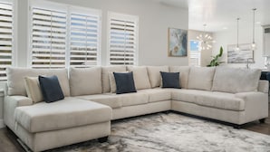 A modern living room with a beige sectional sofa, a marble-patterned rug, and white shutters on the windows. - Family Oasis Getaway (Lehi)