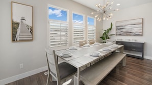 A dining area with a long table set for six, white walls, a large window, and a modern chandelier. - Family Oasis Getaway (Lehi)