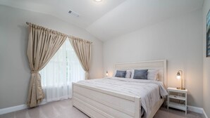 Une chambre à coucher avec un lit, des rideaux, une table de chevet et une lampe.