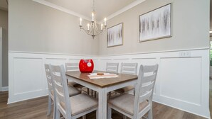 Un coin repas avec une table en bois, des chaises à revêtement blanc, un vase rouge et un lustre.