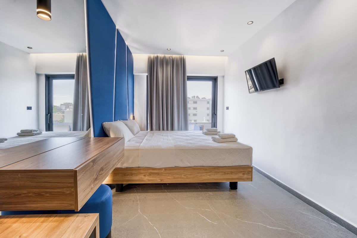 A modern hotel room with a large bed, a wooden desk, a flat-screen TV, and large windows with curtains.