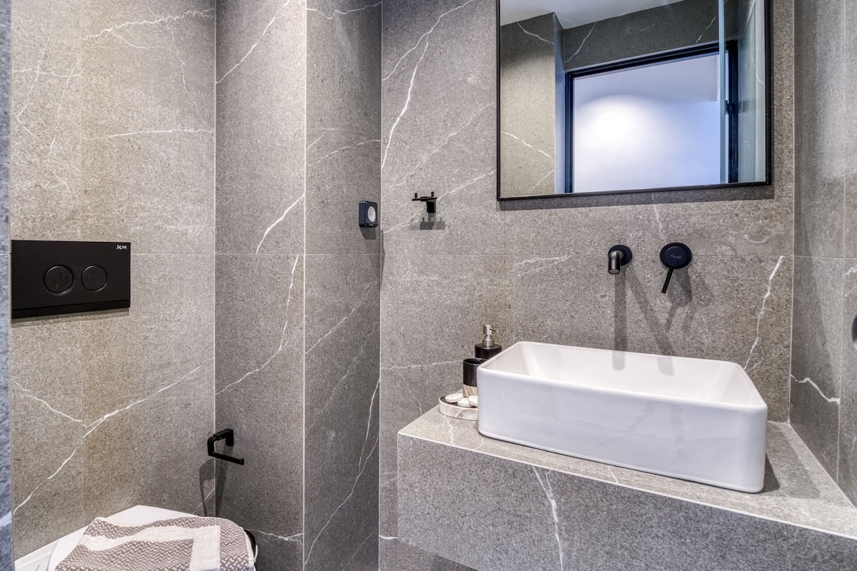 A modern bathroom with a rectangular sink, a mirror above it, and a shower area with a control panel.