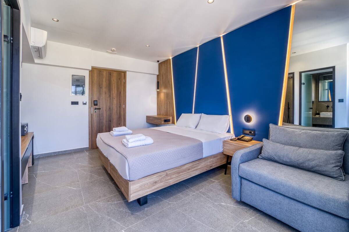 A modern hotel room with a large bed, a seating area, and a bathroom visible through a glass door.