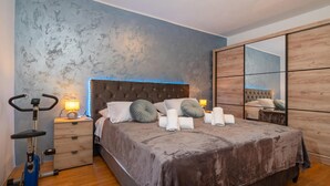A bedroom with a large bed, a nightstand with a lamp, a wall-mounted exercise bike, and a mirror. - Gorgeous home in Pridraga with WiFi (Pridraga)