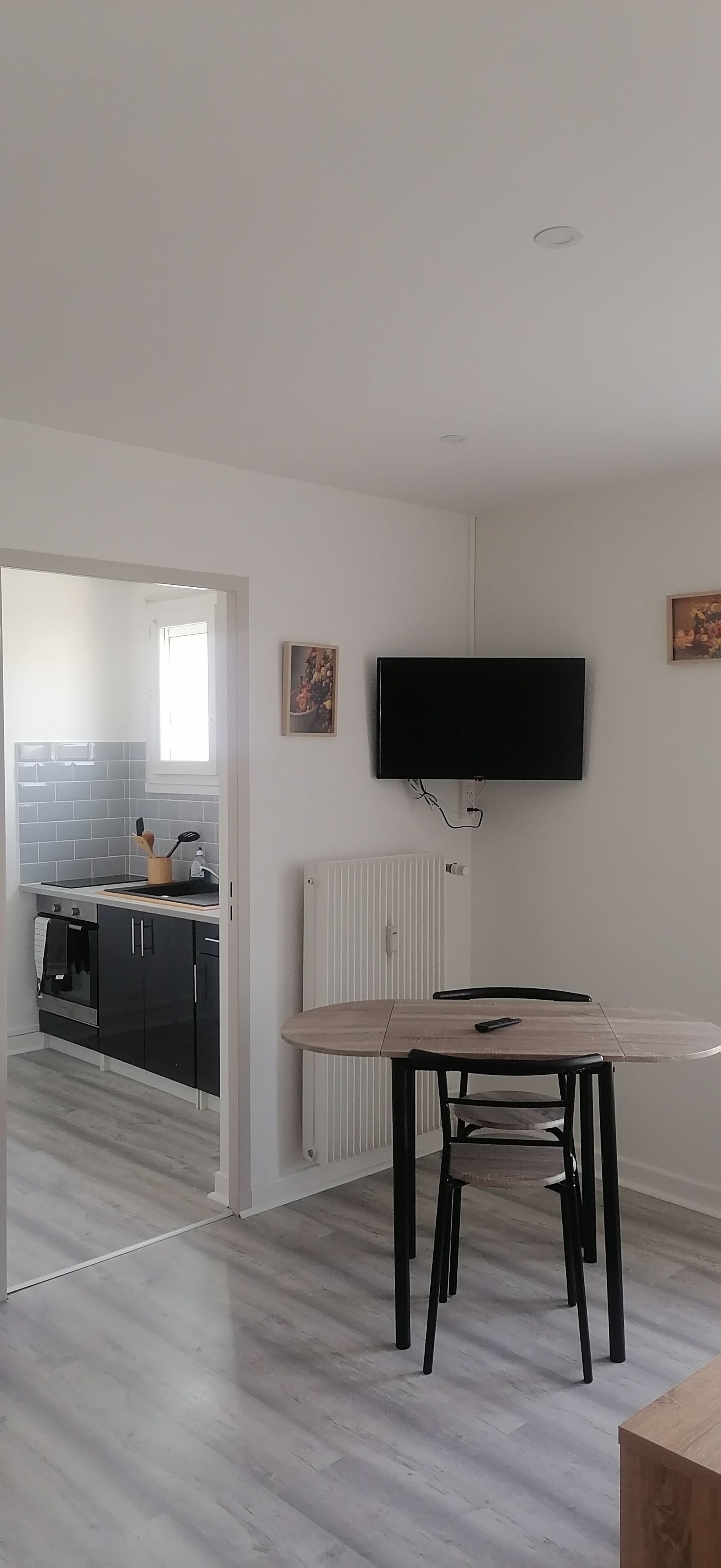 A modern kitchen with a built-in oven, a dining area with a table and chairs, and a flat-screen TV mounted on the wall.