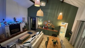 Un salon moderne avec une cheminée, des murs verts et un coin repas comprenant une table et des chaises en bois.