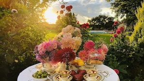 Une table dressée à l’extérieur, ornée d’un assortiment de fleurs, de fruits et d’une théière.