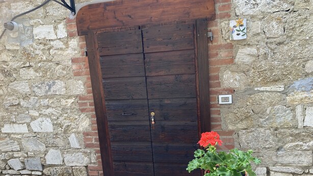 A rustic wooden door with a metal handle, set in a stone wall with a brick base. - Entire apartment in the heart of Tuscany, between Val di Chiana and Val d'Orcia. (Sinalunga)