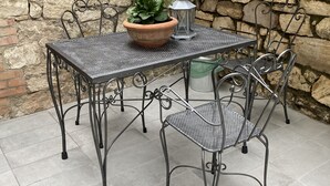 A stone wall, a metal table with chairs, a potted plant, and a lantern. - Entire apartment in the heart of Tuscany, between Val di Chiana and Val d'Orcia. (Sinalunga)