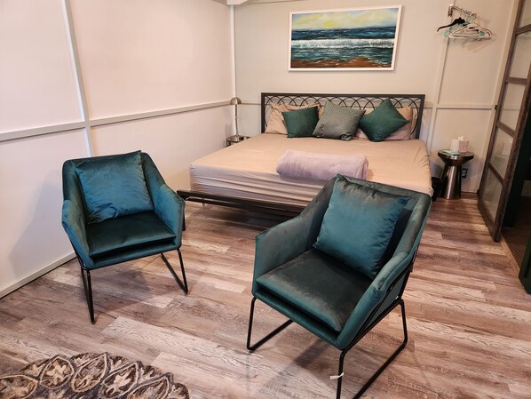 A bedroom with a bed, two chairs, a painting, and a small table. - Downtown Cottage (St. Augustine)