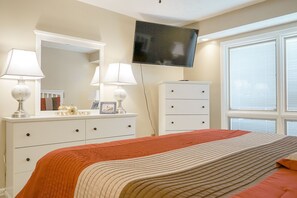 Un dormitorio con cama, cómoda, televisor y ventana con persianas.