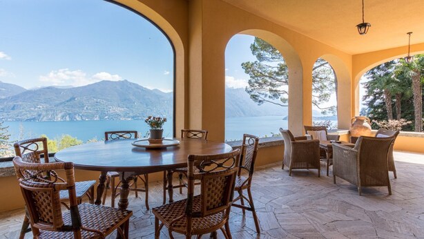 A dining area with a table and chairs, large arched windows, and a view of mountains and water. - Villa Gaia Luxury Retreat with Private Pool in Menaggio (Menaggio)