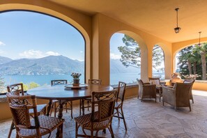 A dining area with a table and chairs, large arched windows, and a view of mountains and water. - Villa Gaia Luxury Retreat with Private Pool in Menaggio (Menaggio)