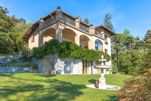 A two-story house with a stone facade, arched windows, and a fountain in the front yard.