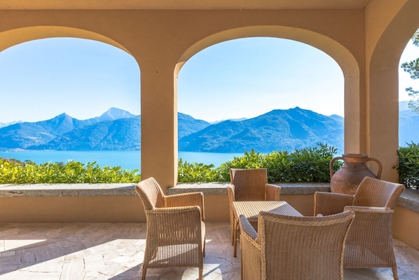 A terrace with wicker furniture, a vase, and a view of mountains and sea.