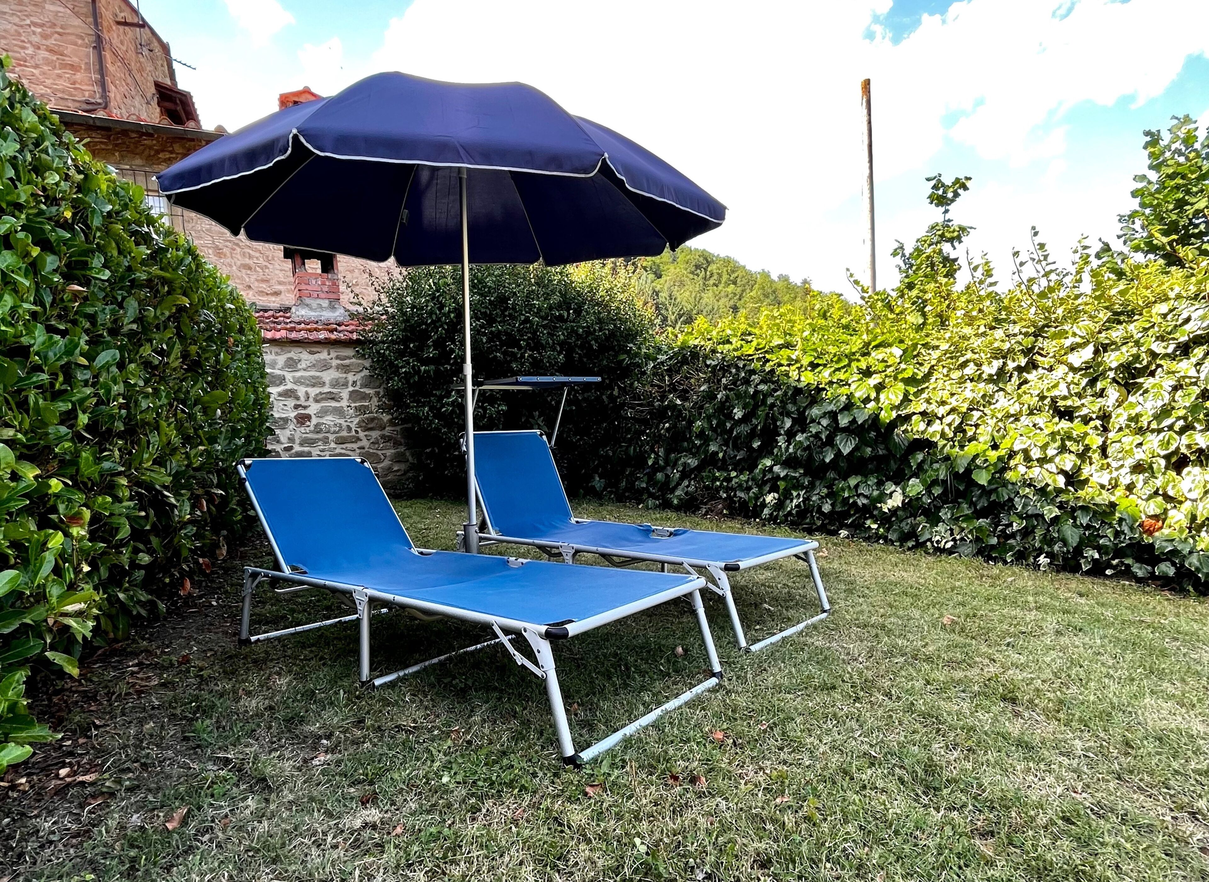Ein Garten mit zwei blauen Liegestühlen und einem großen, blauen Sonnenschirm.