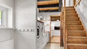 A laundry room with a washing machine, a drying rack, and a wooden staircase leading to a kitchen area. - 3 bedroom cozy home in Bindslev (Bindslev)