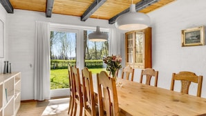 A dining area with a wooden table and chairs, large windows, and a view of a garden. - 3 bedroom cozy home in Bindslev (Bindslev)