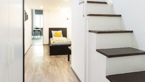 Una escalera de madera con paredes blancas que lleva a un dormitorio con cama y almohada amarilla.