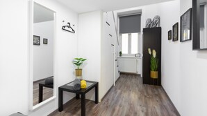 Un pasillo con suelo de madera, una mesa negra con toallas, una planta en maceta y un espejo.