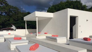 Una terraza en la azotea con varias zonas de estar blancas, cada una con un colchón y una toalla enrollada.