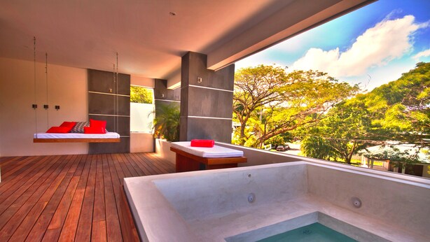 A modern spa room with a wooden floor, a large bathtub, and a seating area with red cushions. - Guest Friendly- 20% off for Bookings in 2024 (Sosua)