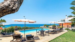 A poolside area with lounge chairs, umbrellas, and a view of the ocean.