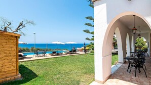 A poolside area with a view of the ocean, outdoor seating, and a covered patio.