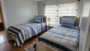 Quarto com duas camas de solteiro, piso de madeira, luminária no teto e janela com cortinas.