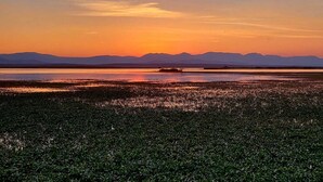Um pôr do sol sobre uma paisagem plana, com montanhas ao longe.