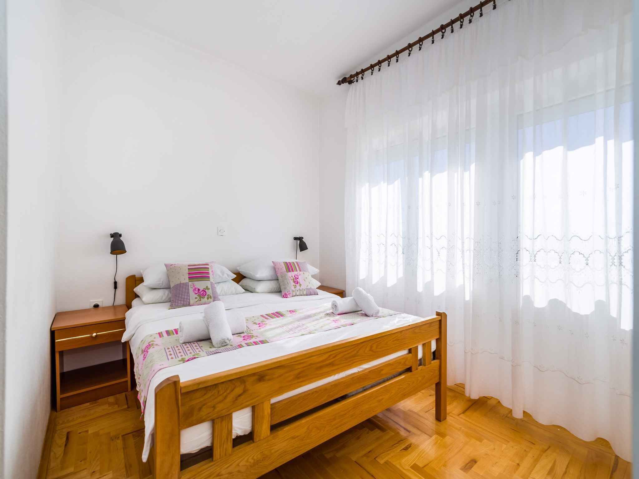 A bedroom with a wooden bed, white bedding, a nightstand with a lamp, and sheer curtains.