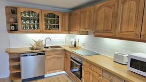 A kitchen with wooden cabinets, a dishwasher, an oven, a sink, and a microwave. - Modernes Wohnenauf dem Land (Langsur)