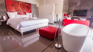 Ein modernes Hotelzimmer mit einem großen Bett, einem roten Hocker, einer weißen Badewanne und einem roten Sofa.