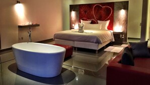 Ein modernes Schlafzimmer mit einer großen Badewanne, einem Bett mit einem herzförmigen Kopfteil und zwei Nachttischlampen.