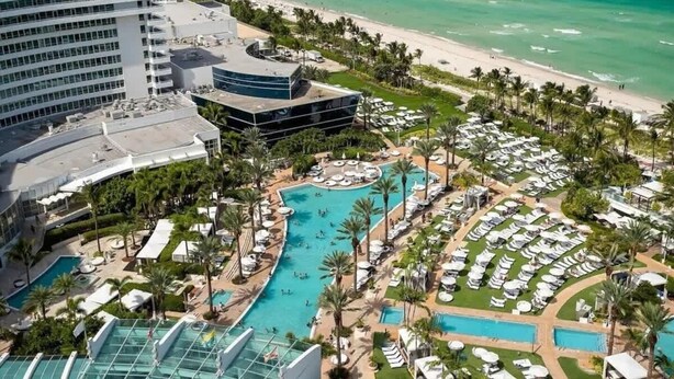 A resort with multiple swimming pools, a beach, and a large hotel building.
