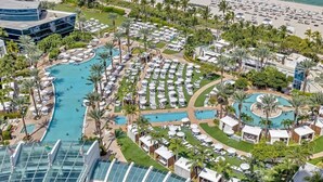 An aerial view of a resort with multiple swimming pools, sun loungers, and a beach area.