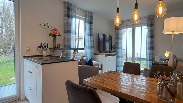 A modern kitchen with a central island, a dining area with a wooden table, and a living space with a TV. - Schwedengang 7A Whg.1 Unten Links (Zingst)